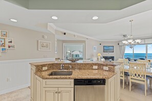 A kitchen with a granite countertop, dishwasher, and a dining area with a view of the ocean. - Belmont Towers 502 by Seaside Vacations & Sales (Ocean City)