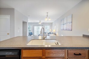 A kitchen with a granite countertop, stainless steel sink, wooden cabinets, and a dining area in the background. - Captain View Villa 3 by Seaside Vacations & Sales (Ocean City)