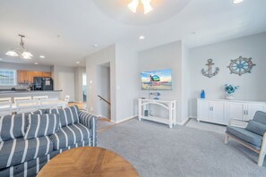 A modern living room with a sofa, a coffee table, and a television. There is a kitchen area with cabinets and a refrigerator. - Captain View Villa 3 by Seaside Vacations & Sales (Ocean City)