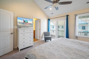 Un dormitorio con cama, cómoda, televisor, ventilador de techo y vistas al exterior.