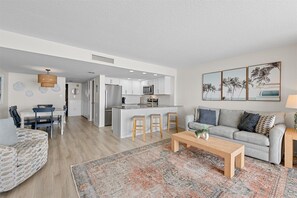 A modern living room with a grey sofa, a coffee table, and a patterned rug. - Fountainhead Towers 1604 by Seaside Vacations & Sales (Ocean City)