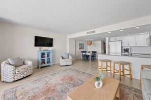 A modern living room with a sofa, a coffee table, and a dining area with chairs and a rug. - Fountainhead Towers 1604 by Seaside Vacations & Sales (Ocean City)