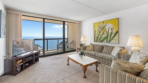 Sala de estar com uma televisão grande, um sofá, uma mesa de centro e vista para o oceano.