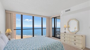 Quarto com cama grande, cômoda e vista para o mar.