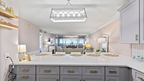 Een moderne keuken met een centraal eiland, grijze kastjes met gouden handgrepen en een hanglamp.