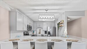 Een moderne keuken met witte kasten, een centraal keukenblok met barkrukken en een hanglamp.