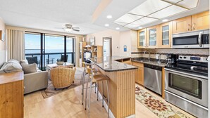 A modern kitchen with stainless steel appliances, a bar area, and a view of the ocean. - Ocean View condo w/ 3 pools by Seaside Vacations & Sales (Ocean City)