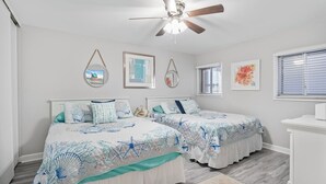 Ein Schlafzimmer mit zwei Betten, einem Deckenventilator und gerahmten Bildern an der Wand.