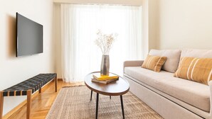 A modern living room with a sofa, a coffee table with books, a TV mounted on the wall, and a bench. - The MP10 Residence - Kolonaki (Athens)