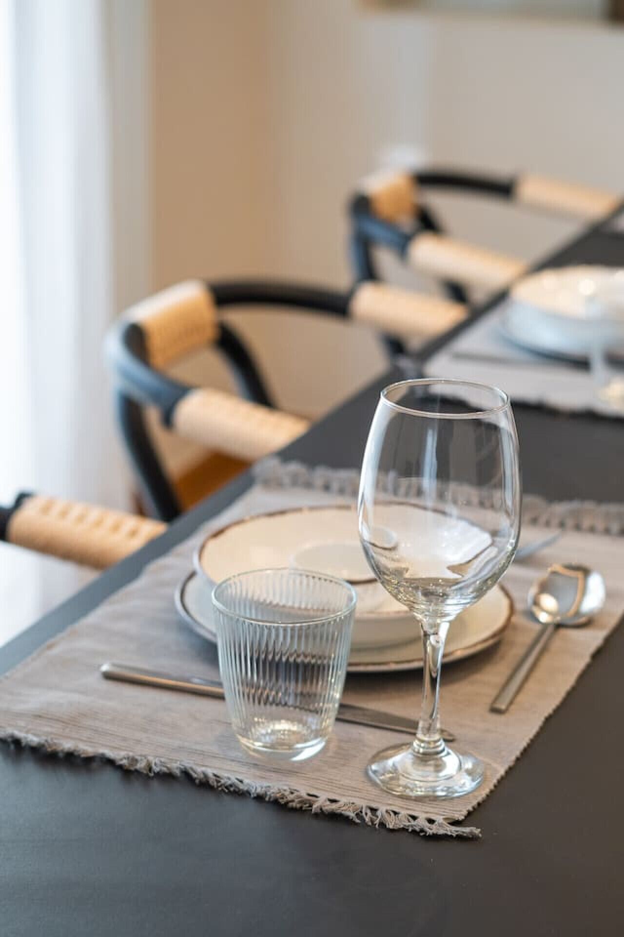 Una mesa de comedor dispuesta con un vaso transparente, un vaso acanalado y un plato, con un mantel individual y un cuchillo sobre la mesa.