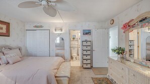 Een slaapkamer met een bed, een dressoir, een spiegel en een plafondventilator.