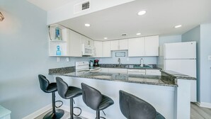 A modern kitchen with white cabinets, a granite countertop, and black bar stools. - Sea Gate 202 by Seaside Vacations & Sales (Ocean City)