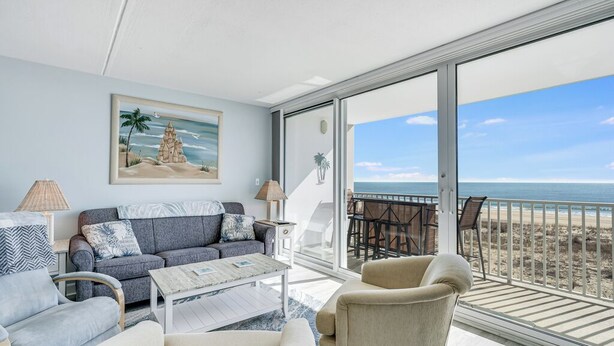 A modern living room with a large window overlooking a beach. - Sea Gate 202 by Seaside Vacations & Sales (Ocean City)
