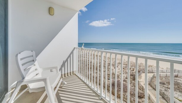 A balcony with a white railing, a white plastic chair, and a view of the beach. - Ocean view condo Seaside Vacations & Sales (Ocean City)