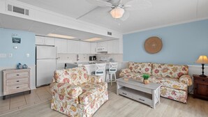 Un espacio habitable compacto con kitchenette, dos sofás estampado de flores, una pequeña mesa y un ventilador de techo.