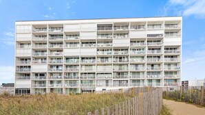 Un hotel de varios pisos con balcones, situado cerca de una zona de playa de arena.