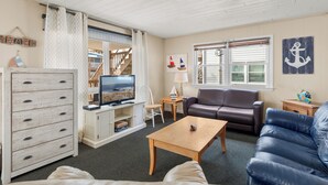 A living room with a TV, a wooden coffee table, a brown leather sofa, and a white cabinet. - Seas the Day 1 by Seaside Vacations & Sales (Ocean City)