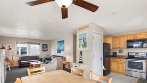 A spacious kitchen with wooden cabinets, a stainless steel refrigerator, and a double oven. There is a dining area with a wooden table and chairs. - Seas the Day 1 by Seaside Vacations & Sales (Ocean City)