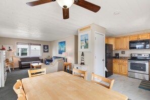 A spacious kitchen with wooden cabinets, a stainless steel refrigerator, and a double oven. There is a dining area with a wooden table and chairs. - Seas the Day 1 by Seaside Vacations & Sales (Ocean City)