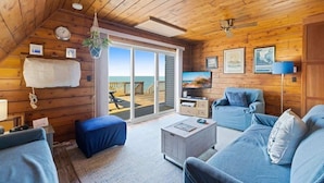 L’intérieur d’un chalet en bois, avec un balcon, un canapé, une table basse et une plante suspendue.