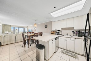Una cocina moderna con armarios blancos, una isla central y un comedor con mesa y sillas.