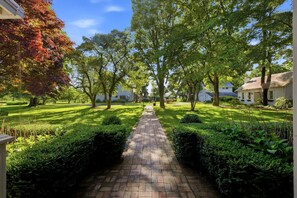 A paved pathway leading through a well-maintained garden with mature trees and neatly trimmed hedges. - Juniper Presents: The Farmhouse at Historic 33 Acre Berrywood Farm (Three Oaks)