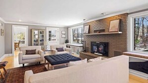 Ein Wohnzimmer mit Kamin, einer Couch, einem Couchtisch und einem Essbereich im Hintergrund.