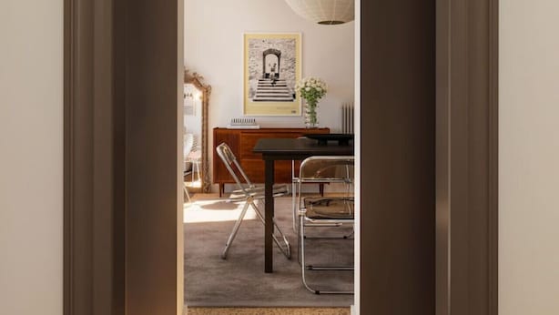 En hall som leder till en matplats med ett bord och stolar, en inramad tavla på väggen och en dekorativ lampa.