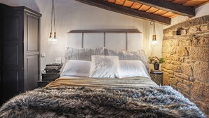 A bedroom with a wooden ceiling, stone wall, and a bed with a fur throw.