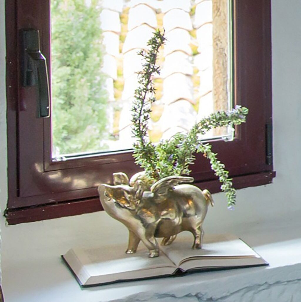 Une fenêtre donnant sur un paysage verdoyant, une sculpture décorative en laiton représentant un éléphant, et un livre ouvert posé sur une surface en marbre.