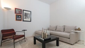 Un salon moderne avec un fauteuil rouge, un canapé gris, une table basse noire et une petite table d’appoint blanche.