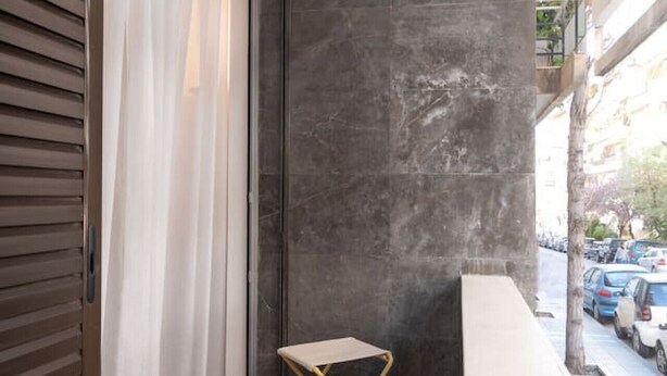 Un petit balcon donnant sur des voitures garées, une porte-fenêtre coulissante et un mur sombre à la texture marquée.
