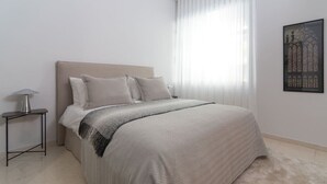 Une chambre à coucher avec un lit, une table de chevet, une lampe et une fenêtre avec des rideaux légers.