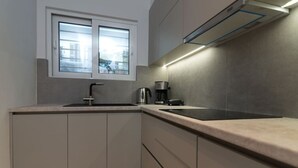 Une cuisine moderne équipée d’une cuisinière intégrée, d’une machine à café et d’une fenêtre avec des stores.