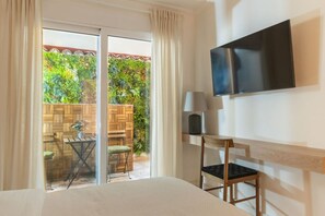 Habitació d'hotel amb llit, televisió penjada a la paret, taula petita amb làmpada i porta corredissa de vidre que dona a zona exterior amb taula i cadires de fusta.