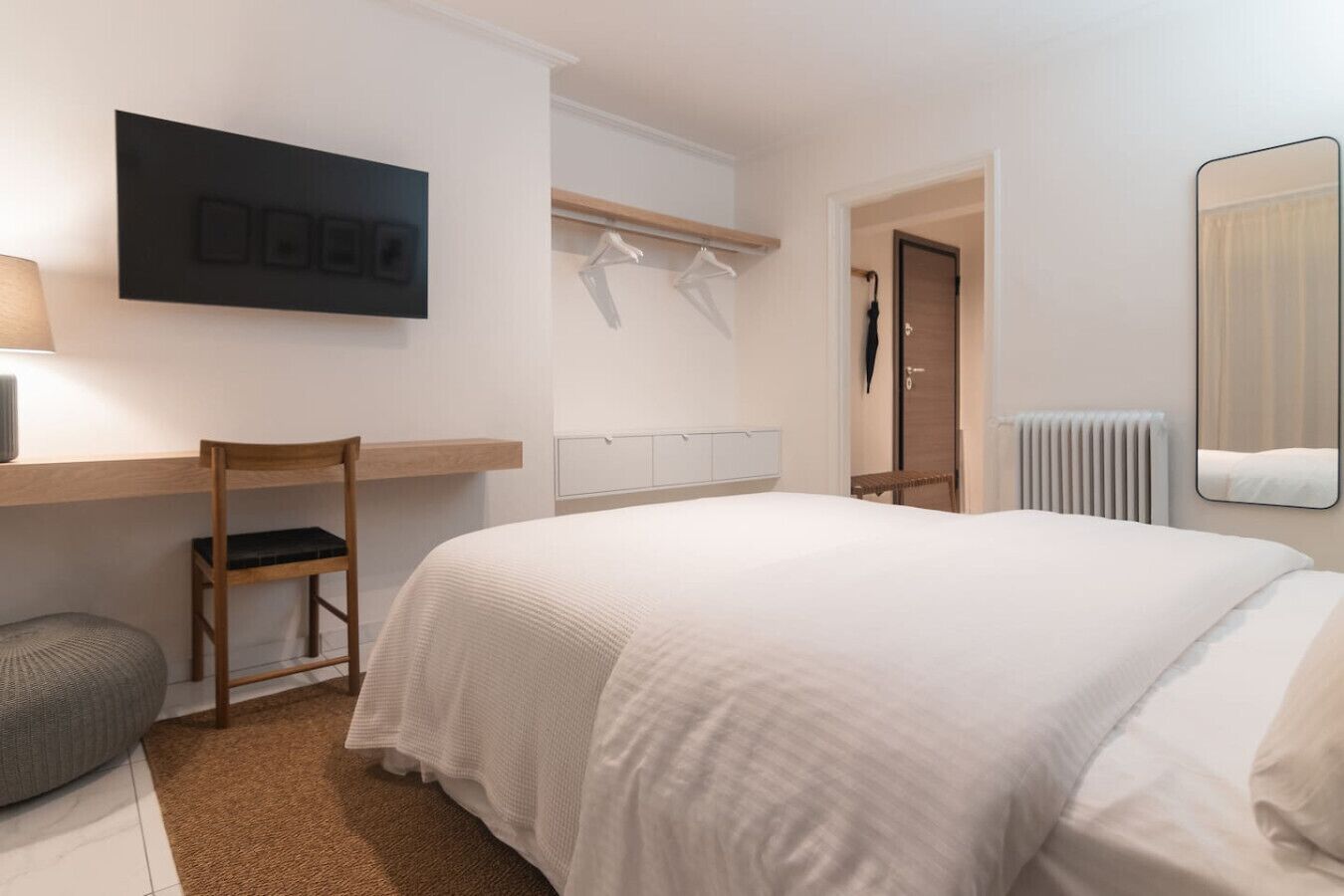 Ein Hotelzimmer mit Bett, Stuhl, Schreibtisch, Fernseher, Kleiderständer und Heizkörper.