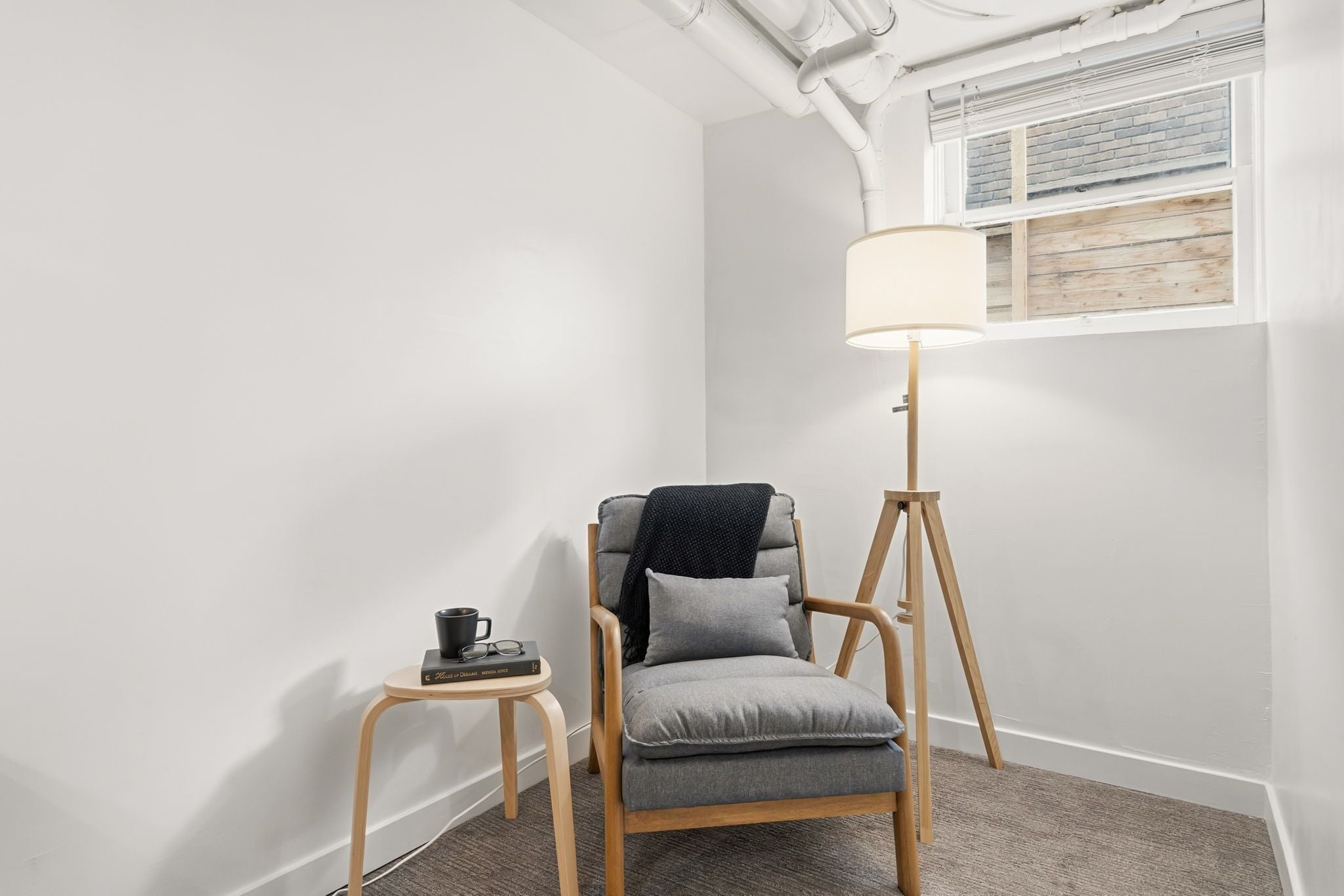 Une pièce moderne avec un fauteuil gris, une lampe sur pied et une petite table sur laquelle se trouvent une tasse et des livres.