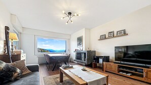 Ein modernes Wohnzimmer mit großem Fernseher, Holzmöbeln, einem Kamin und Blick auf eine Berglandschaft.