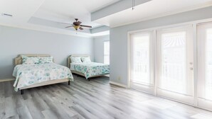 Une chambre avec deux lits, un ventilateur de plafond et de grandes portes-fenêtres coulissantes.