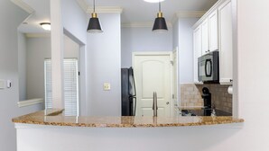 Une cuisine dotée d’un plan de travail en granit, de meubles blancs, d’un réfrigérateur noir et de luminaires suspendus.