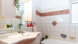 Un bany modern amb un lavabo gran, un mirall i una banyera. Hi ha elements decoratius a la paret i un penjador de tovalloles.