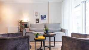 Un saló modern amb un sofà gris, dues butaques, una taula auxiliar amb llibres i una planta, i un radiador.