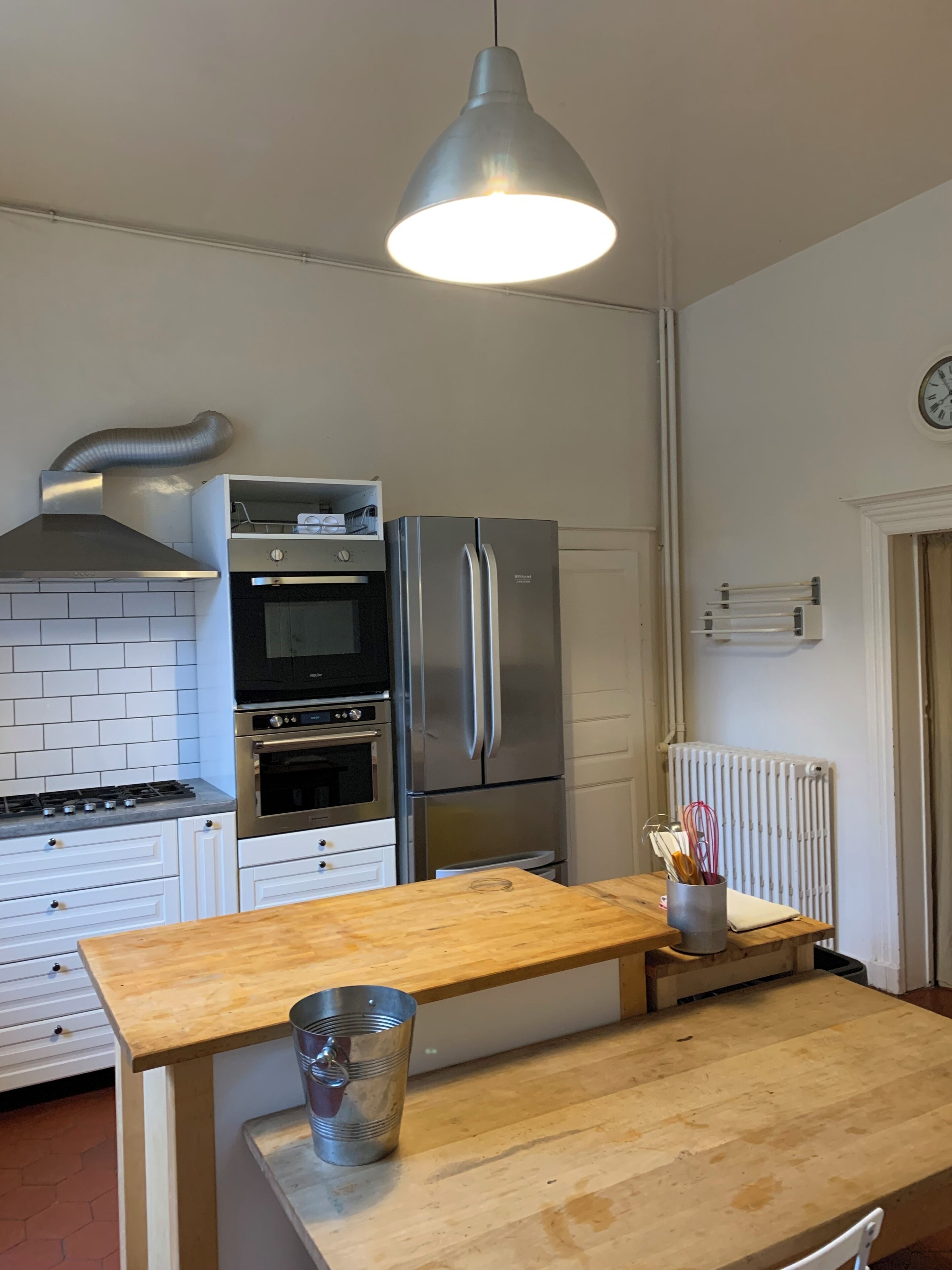 Een moderne keuken met een roestvrijstalen koelkast, oven en magnetron. Er staat een houten tafel met een metalen bak erop.