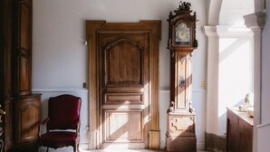 A room with a wooden door, a red chair, a tall wooden clock, and a staircase leading to another level. - Domaine de Vauluisant, gîte for 32 people in Burgundy (COURGENAY)