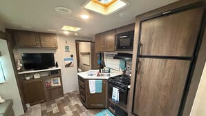 Een kleine keuken met houten kastjes, een inbouwmagnetron, een kookplaat en een spoelbak.