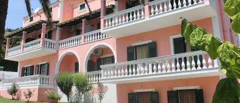 Un edificio rosa de varios pisos con balcones, arcos y un césped bien cuidado.