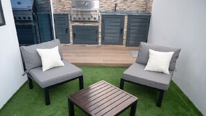 A patio with two grey sofas, a wooden table, and a barbecue grill in the background.