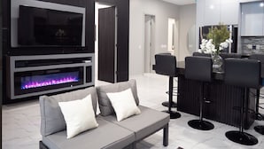 A modern living room with a flat-screen TV, a fireplace, a grey sofa, and a bar area with stools.