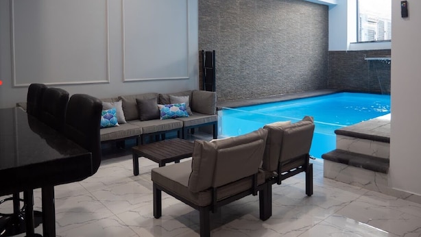 A modern indoor pool area with a sofa and chairs, a pool table, and a stone wall.