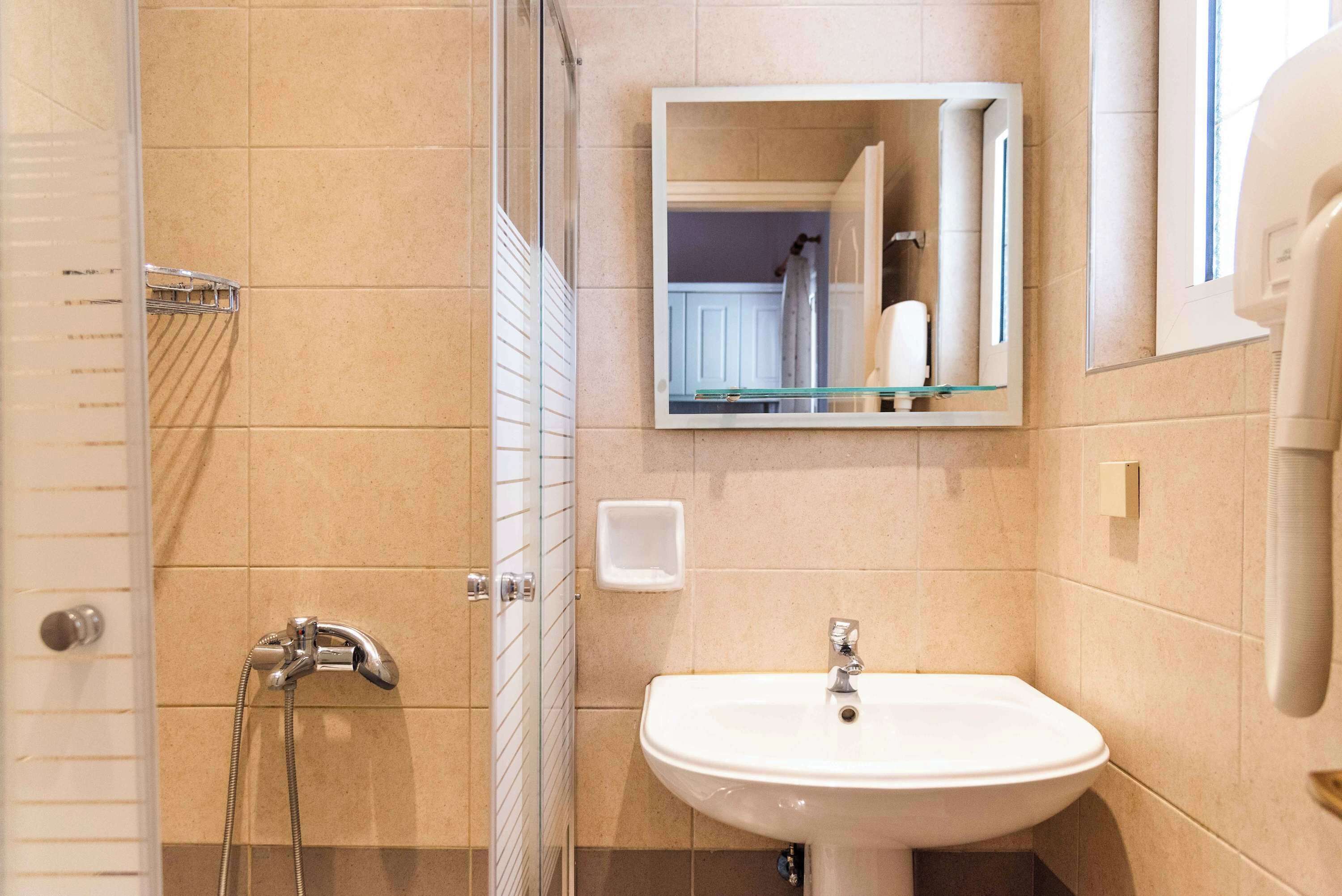 Un baño con cabina de ducha de vidrio, un lavamanos blanco y un espejo sobre él.